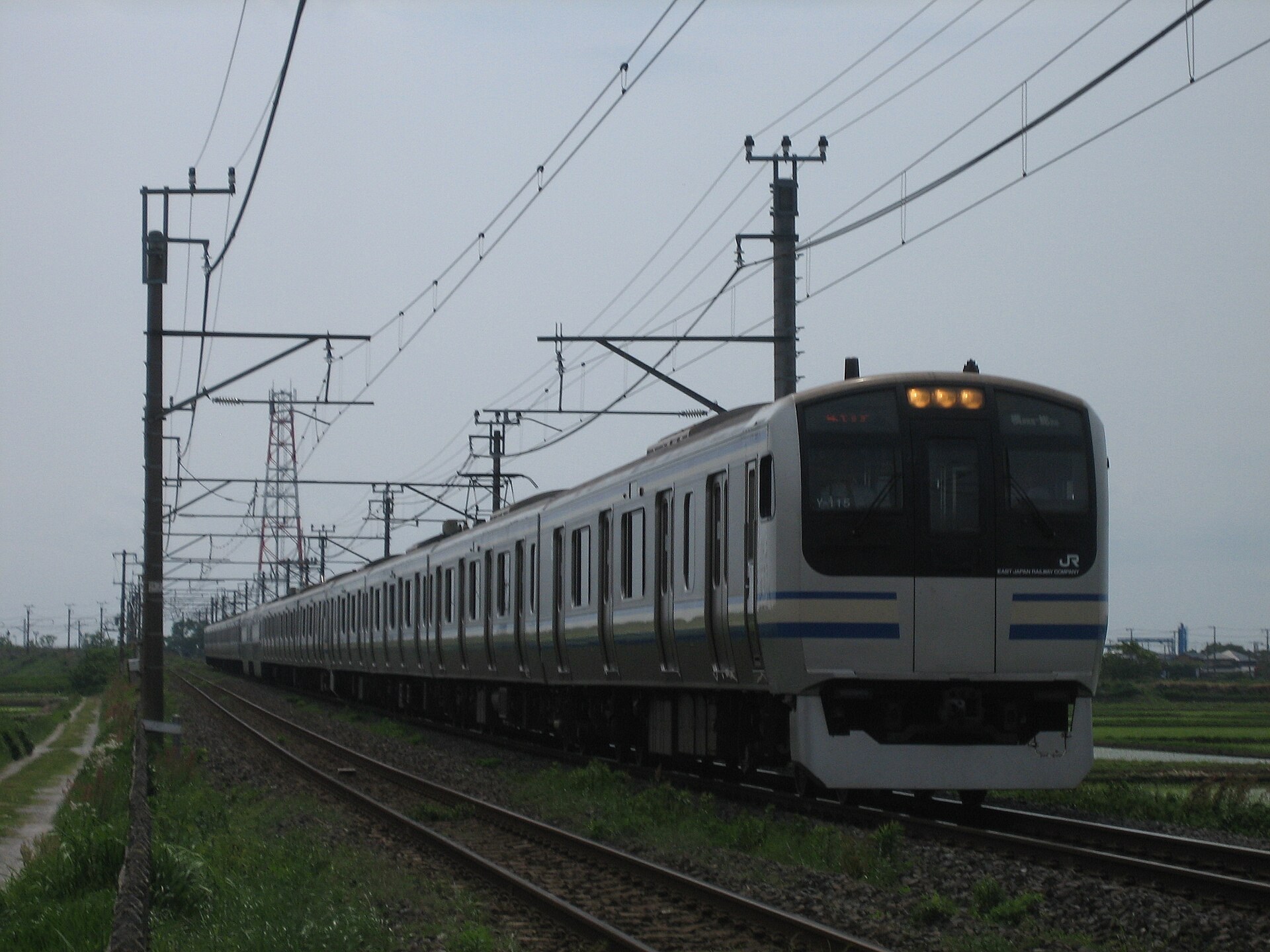 日本大型巴士停泊於車站平台，背景為鐵軌及山丘