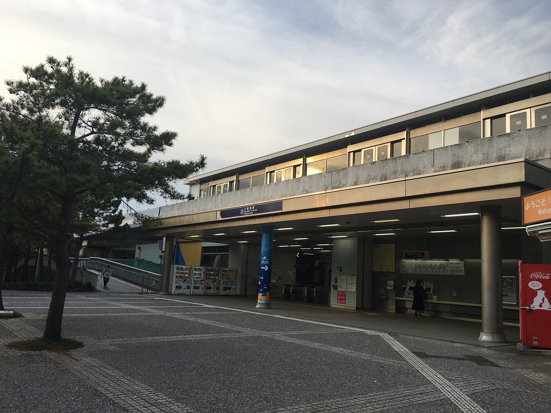 東京灣鐵路車站月台，一班電車停靠，乘客橋橫跨線路上方