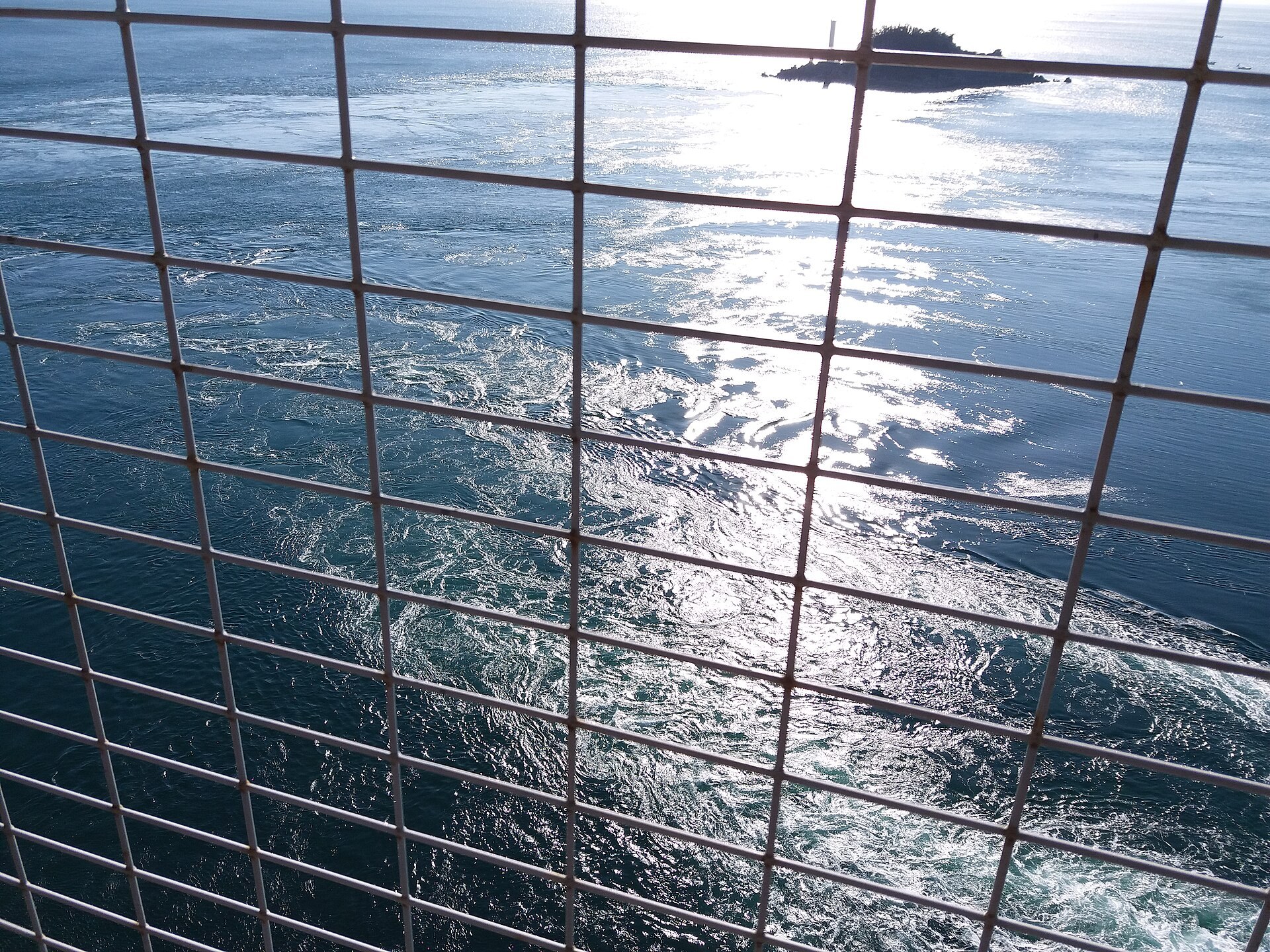 鳴門海峽冬季海面上的巨大渦潮，遠處有帆船航行的剪影