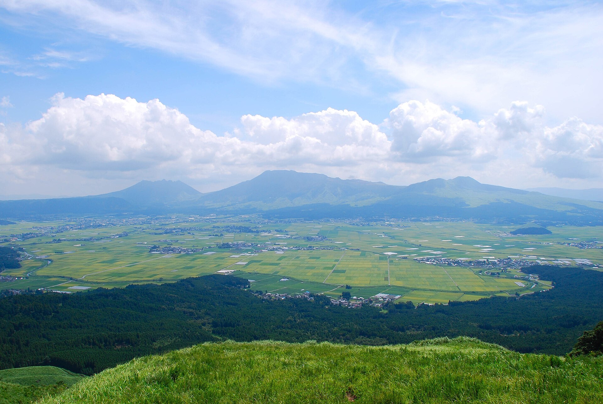 阿蘇火山口背景，一列觀光列車穿過阿蘇高原（示意圖）