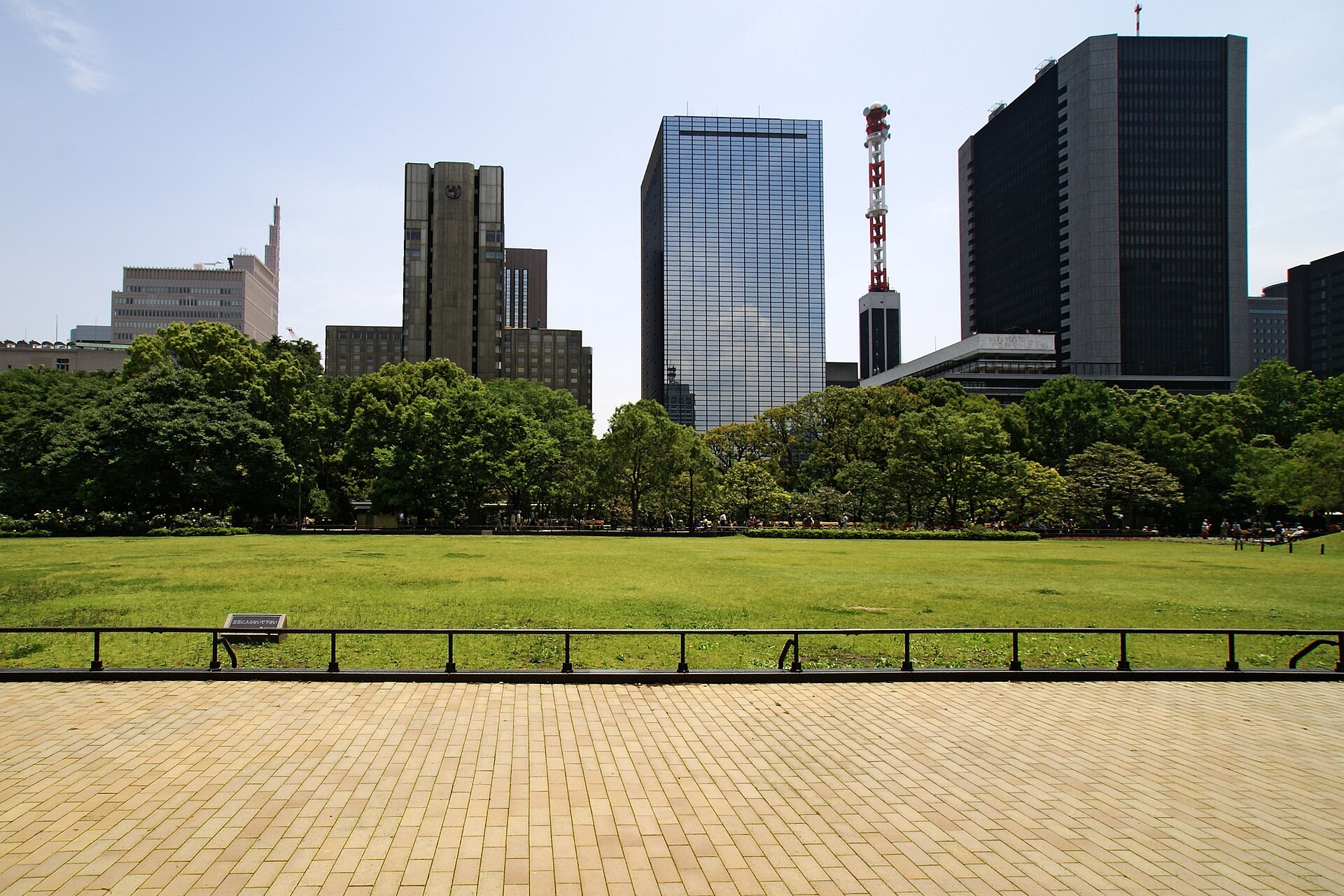 日比谷公園芝庭廣場嘅大片草地，背景係東京都市天線同樹影